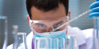 Scientist pipetting blue liquid into test tubes.