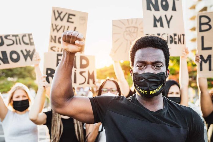 Protester raises fist, wears mask, signs in background.