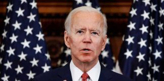 Man speaking at podium with American flags behind