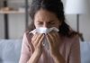 Woman sneezing into a tissue indoors.