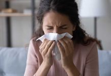 Woman sneezing into a tissue indoors.