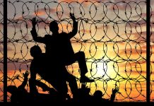 Silhouetted people climbing barbed wire fence sunset background