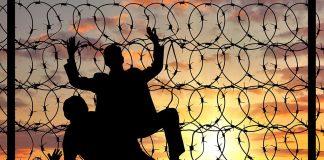 Silhouetted people climbing barbed wire fence sunset background