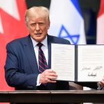 Man holding signed agreement with flags in background