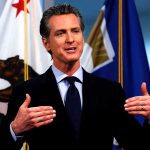 Man speaking in front of California flag backdrop