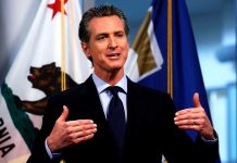 Man speaking in front of California flag backdrop