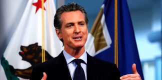 Man speaking in front of California flag backdrop