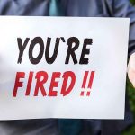 Person holding "YOU'RE FIRED" sign.