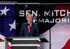 Man speaking at podium with American flag backdrop.