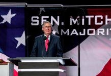 Man speaking at podium with American flag backdrop.