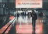 Airport sign: "All Flights Canceled", passengers walking.