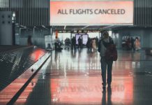 Airport sign: "All Flights Canceled", passengers walking.