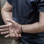 Person handcuffed standing by a vehicle