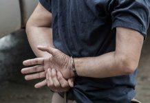 Person handcuffed standing by a vehicle