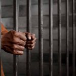 Person gripping metal jail bars tightly