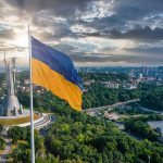 Ukrainian flag flying near city with statue monument
