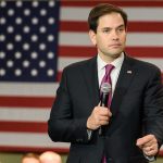 Man holding microphone in front of American flag