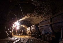 Dimly lit mine shaft with rail carts and tracks.