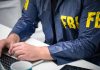 Person in FBI jacket typing on a laptop.