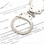 Handcuffs on top of an arrest warrant document