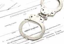 Handcuffs on top of an arrest warrant document