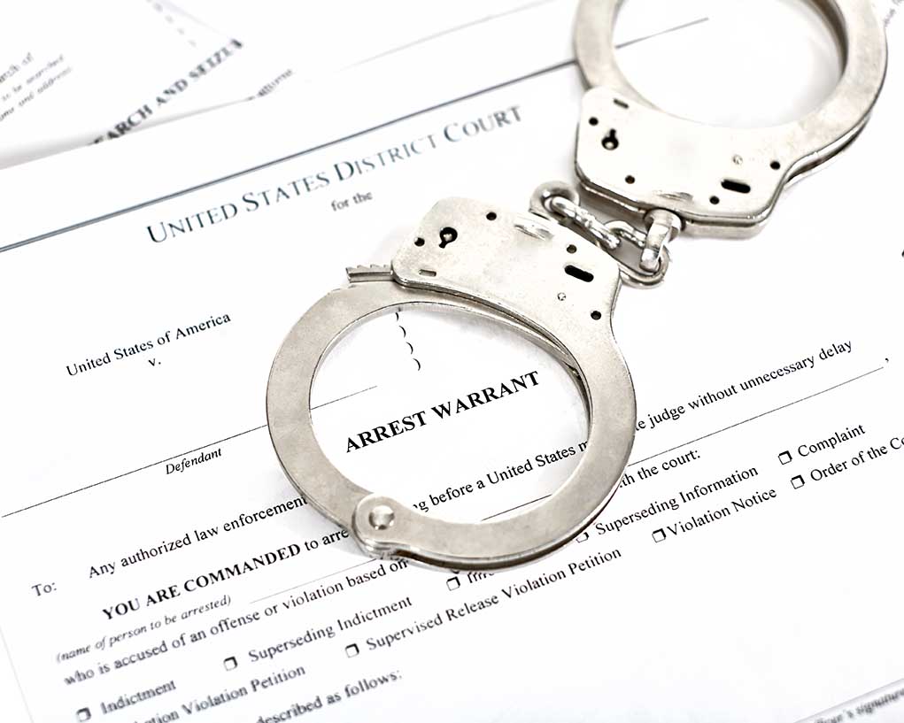 Handcuffs on top of an arrest warrant document