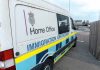 White immigration enforcement van parked by roadside near airport