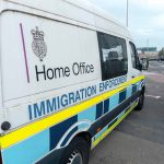 White immigration enforcement van parked by roadside near airport