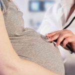 Doctor uses stethoscope on pregnant woman's belly