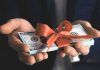 Hands holding stack of hundred dollar bills with ribbon