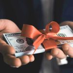 Hands holding stack of hundred dollar bills with ribbon