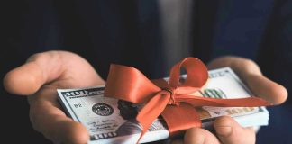 Hands holding stack of hundred dollar bills with ribbon