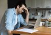 Man stressing over work on laptop at kitchen table.