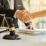 Hands shaking over legal documents with gavel and scales