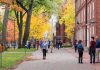 Students walking on a campus path surrounded by autumn trees and brick buildings