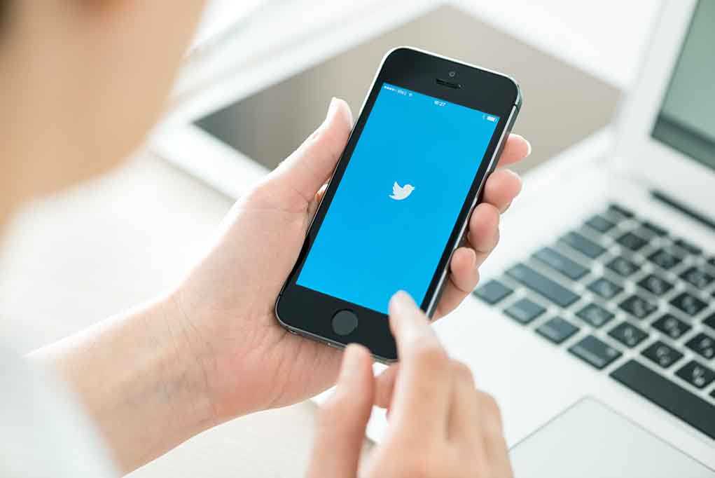 Person holding a smartphone displaying the Twitter app