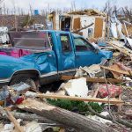 A blue truck surrounded by debris and destruction from a natural disaster
