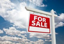 A red For Sale sign against a blue sky with clouds