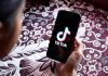 Hand holding phone showing TikTok logo.