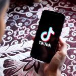Hand holding phone showing TikTok logo.