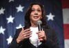 Woman speaking with microphone, American flag background.