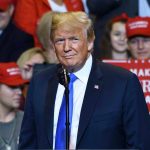 Trump Challenges AOC – IQ Duel Shocks Congress! Person at a rally with Make America Great Again signs.