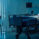 Woman sitting beside hospital bed at night.