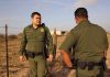 Two uniformed officers standing outdoors near a fence.