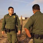 Two uniformed officers standing outdoors near a fence.