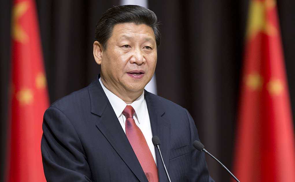 A political leader delivering a speech at a podium with national flags in the background