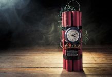 A stick of dynamite with a clock timer and wires, set against a dark smoky background