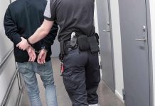 Operation Dirtbag EXPOSED—150 Predators NABBED! Officer escorting handcuffed person down hallway.