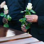 Famous Twins Die Together – Heartbreaking! Mourners holding white roses by a casket.