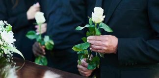 Mourners holding white roses by a casket.